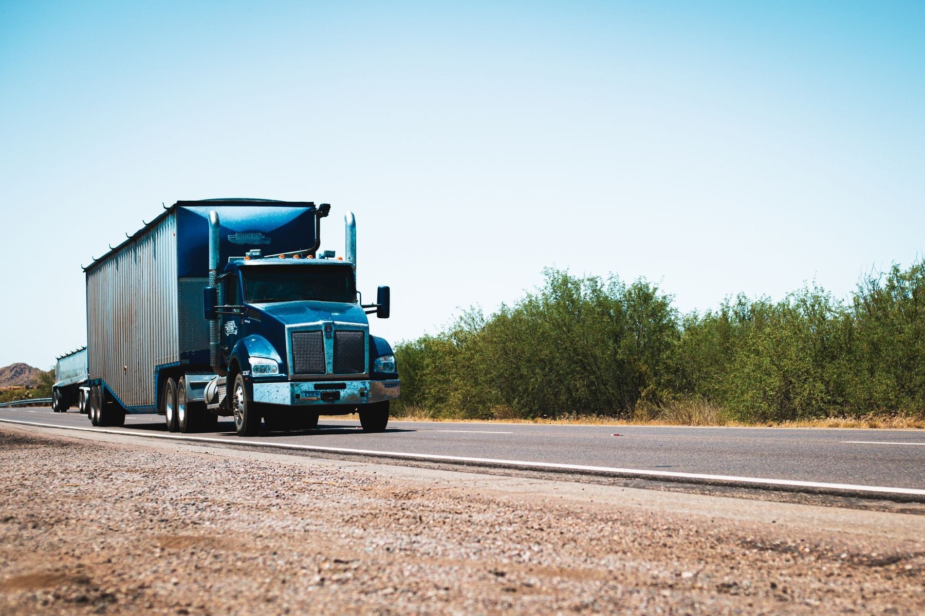Blue conventional semi-truck traveling on a sunlit road