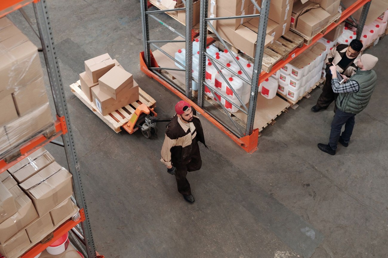 Warehouse workers discussing goods beside pallet racks